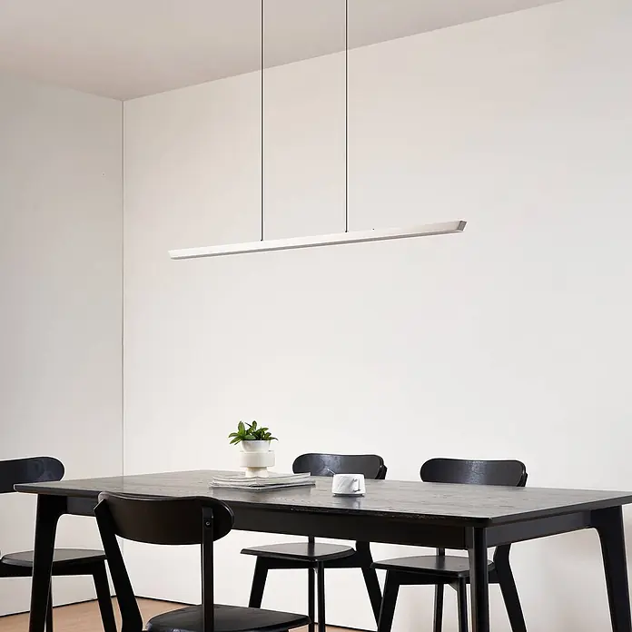Lucande Pendelleuchte Solvar - chrom / silber, silber - Lange, lineare weiße Pendelleuchte über einem dunklen Esstisch mit schwarzen Stühlen.