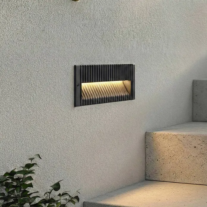 Lucande Außenwandleuchte Tavion - schwarz, schwarz, IP65 - Schwarze rechteckige Einbau-Treppenleuchte mit warmer Beleuchtung, an strukturierter Wand neben Betonstufen.