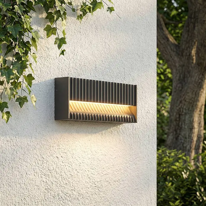 Lucande Außenwandleuchte Tavion - 4,6 x 25 x 10 cm, schwarz, schwarz, IP65 - Dunkelgraue Außenwandleuchte mit vertikalen Lamellen, die warmes Licht nach oben und unten abstrahlt, an einer strukturierten Außenwand montiert.
