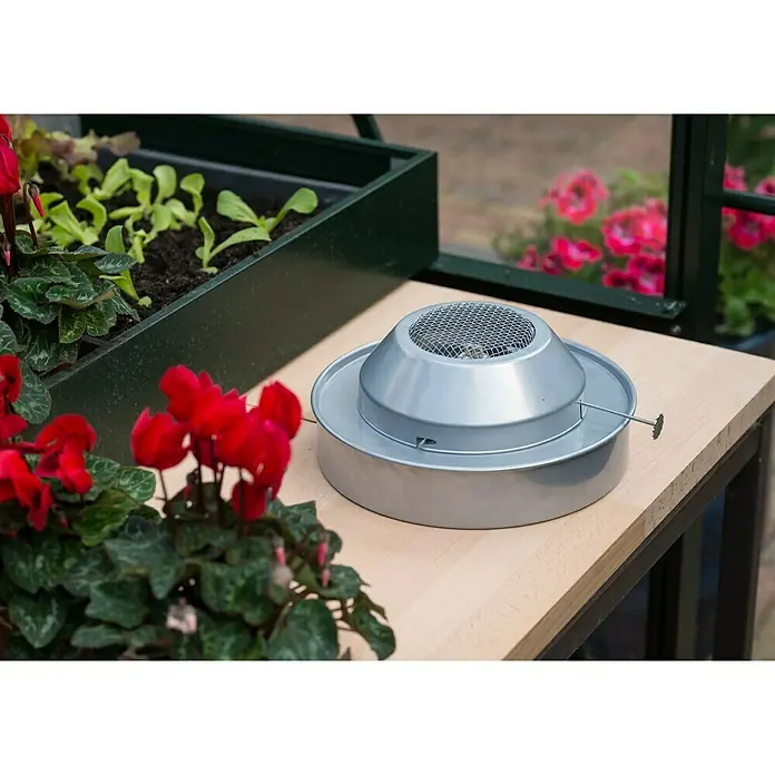 Gewächshaus-Heizung - 21 x 21 x 17 cm - Nahaufnahme einer silbernen Gewächshausheizung auf einem Tisch mit Pflanzen. Ideal zum Schutz von Pflanzen vor Kälte.
