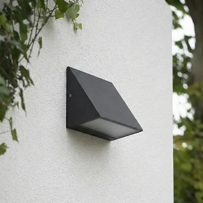 Lindby Außenwandleuchte Triava - schwarz, IP65 - Schwarze, geometrische Außenwandleuchte mit weißem Diffusor, an einer strukturierten Wand montiert.