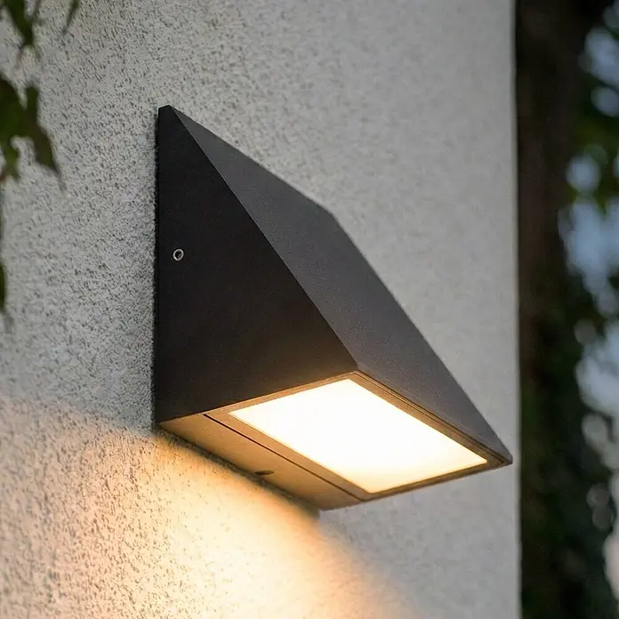 Lindby Außenwandleuchte Triava - schwarz, IP65 - Schwarze, eckige Außenwandleuchte an strukturierter Wand, strahlt warmes Licht nach unten ab.