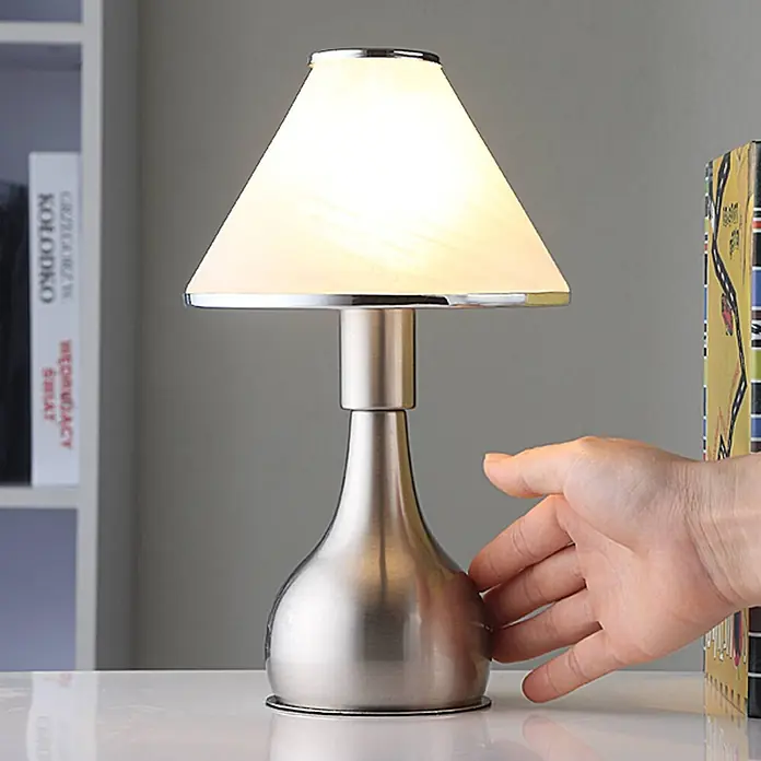Lindby Tischleuchte Ellen - L x B x H: 15 x 15 x 25,5 cm, alu / grau / zink, weiß / opal, E14 - Gebürstete Nickel-Tischlampe mit weißem konischem Schirm, von einer Hand berührt.