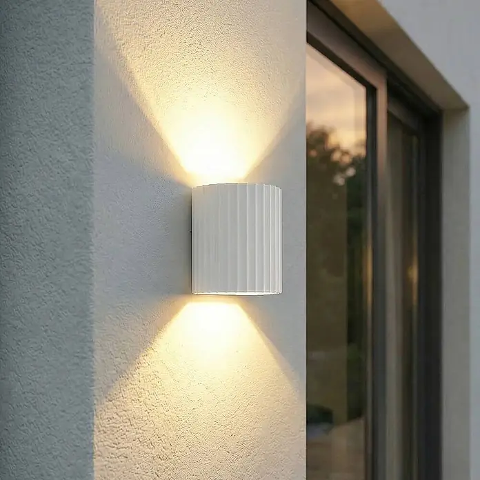 Lindby Außenwandleuchte Ralino - 9,6 x 11 x 11 cm, weiß / opal, weiß / opal, IP65 - Weiß gerippte zylindrische Außenwandleuchte mit warmem Up/Down-Licht an einer Außenwand.