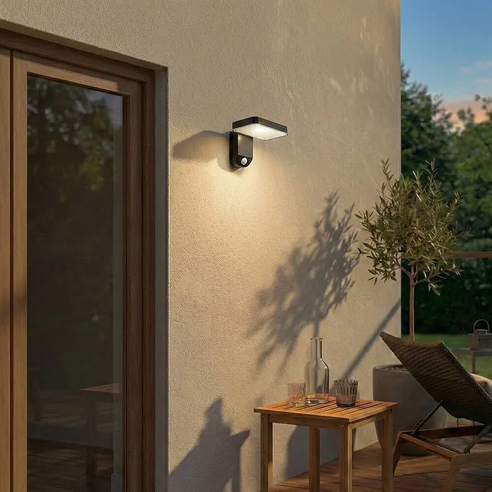 Prios Außenwandleuchte Tarlson - 12,8 x 18 x 12 cm, schwarz, IP44 - Schwarze Außenwandleuchte mit weißem Diffusor und Bewegungsmelder, beleuchtet einen Terrassenbereich.