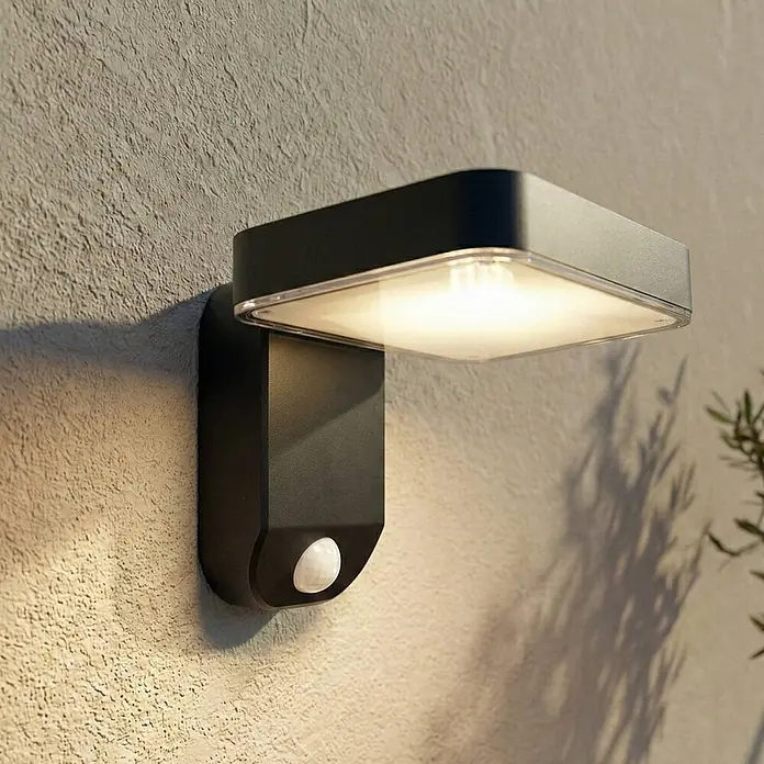 Prios Außenwandleuchte Tarlson - 12,8 x 18 x 12 cm, schwarz, IP44 - Schwarze Außenwandleuchte mit Bewegungssensor, beleuchtet eine strukturierte Wand.