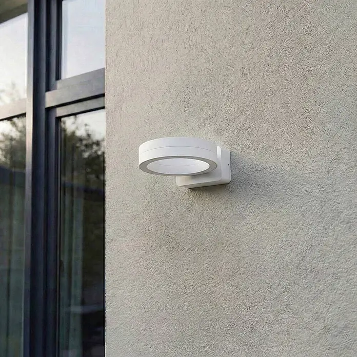 Lindby Außenwandleuchte Selviro - 24,3 x 20 x 10 cm, weiß / opal, weiß / opal, IP65 - Weiße, runde LED-Wandleuchte, an einer strukturierten Wand neben einem Fenster montiert.