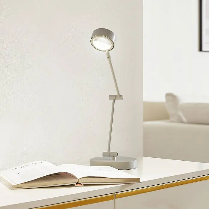 Lindby Tischleuchte Jyla - weiß / opal, weiß / opal - Graue verstellbare Schreibtischlampe mit eingeschaltetem Licht, die ein offenes Buch auf einem weißen Tisch beleuchtet.