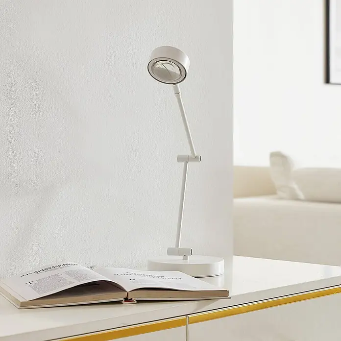 Lindby Tischleuchte Jyla - weiß / opal, weiß / opal - Weiße verstellbare Schreibtischlampe beleuchtet ein offenes Buch auf einem schlichten weißen Tisch.