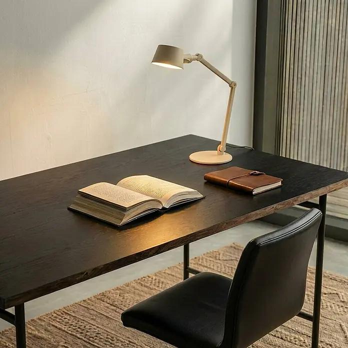 Lucande Tischleuchte Silka - L x B x H: 71 x 22 x 93,5 cm, creme / amber, creme / amber, E27 - Verstellbare hellbeige Schreibtischlampe beleuchtet ein offenes Buch auf einem dunklen Holzschreibtisch. Ein schwarzer Stuhl steht daneben.