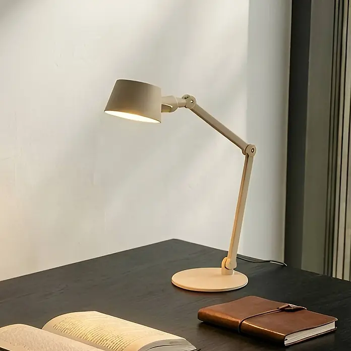 Lucande Tischleuchte Silka - L x B x H: 71 x 22 x 93,5 cm, creme / amber, creme / amber, E27 - Beige verstellbare Schreibtischlampe mit konischem Schirm, beleuchtet einen dunklen Holzschreibtisch mit einem offenen Buch und einem Notizbuch.