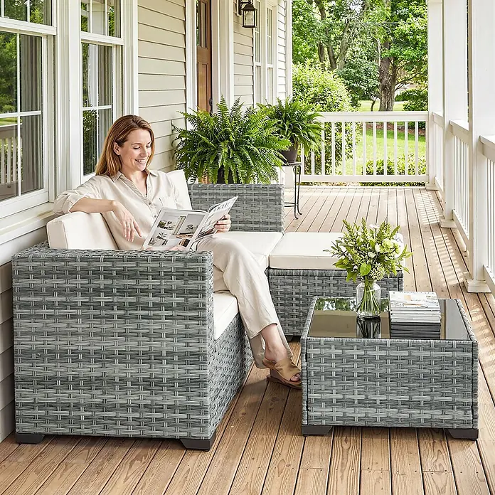 Outsunny Loungemöbel-Set mit Tisch - 5 -tlg., PE-Rattan, Grau - Graues Rattan-Gartensofa mit weißen Kissen und passendem Couchtisch, von einer Frau auf einer Veranda genutzt.