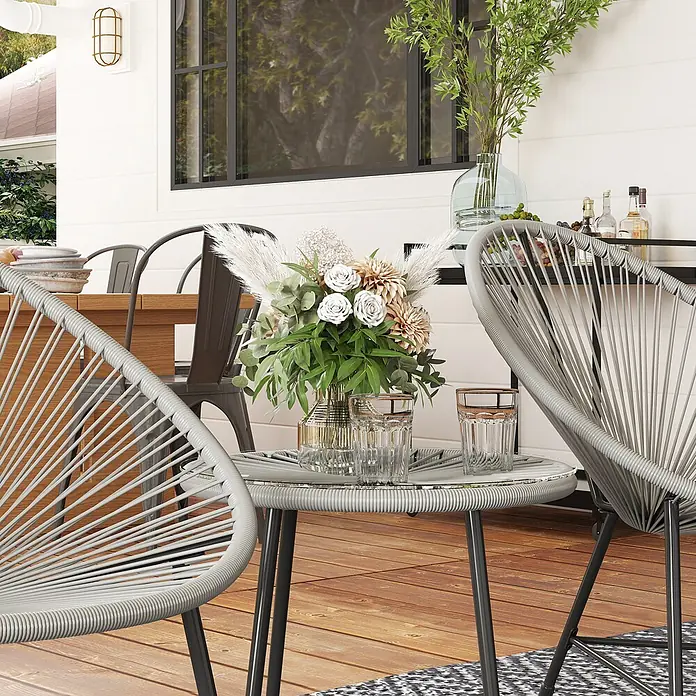 Outsunny Loungemöbel-Set - PE-Rattan, Grau - Graue Outdoor-Stühle aus Kordelgeflecht und ein kleiner runder Tisch auf einer Holzterrasse mit Blumenarrangement.