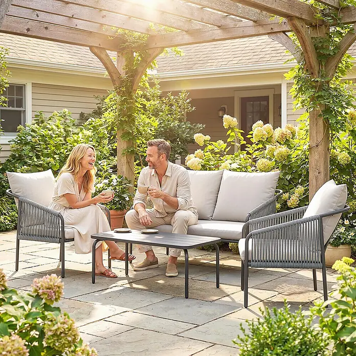 Outsunny Loungemöbel-Set mit Tisch - 4 -tlg., PE-Rattan, Khaki - Outdoor-Sitzgruppe aus grauem Seilgeflecht mit hellen Kissen und dunkelgrauem Couchtisch, von zwei Personen auf sonniger Terrasse unter Pergola genutzt.