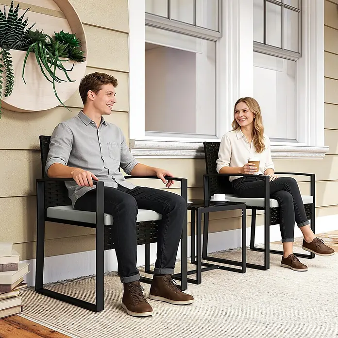 Outsunny Loungemöbel-Set - PE-Rattan, Cremeweiß - Schwarze Metall-Terrassengarnitur: zwei Stühle mit hellen Kissen und ein Glastisch, von einem Paar genutzt.