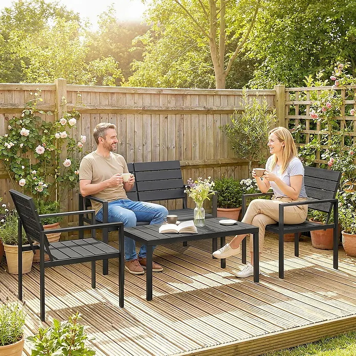 Outsunny Loungemöbel-Set - Polyethylen hoher Dichte (PE‑HD), Schwarz - Dunkelgraue Latten-Gartenmöbel-Set mit Bank, zwei Stühlen und Couchtisch, von zwei Personen im Garten genutzt.