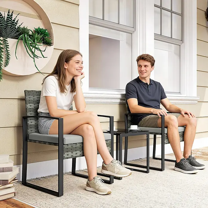 Outsunny Loungemöbel-Set - PE-Rattan, Hellgrau - Zwei Personen entspannen auf einem grauen Rattan- und schwarzen Metall-Bistro-Set mit kleinem Tisch auf einer Terrasse.
