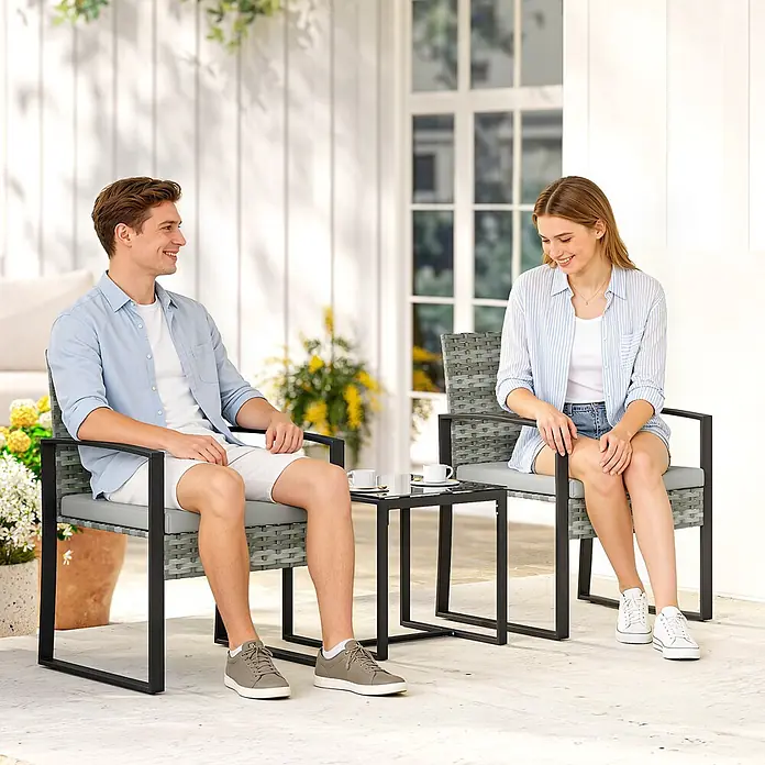 Outsunny Loungemöbel-Set - PE-Rattan, Hellgrau - Graue Polyrattan-Gartengarnitur mit schwarzen Metallrahmen und Glastisch, von zwei Personen auf einer Terrasse genutzt.