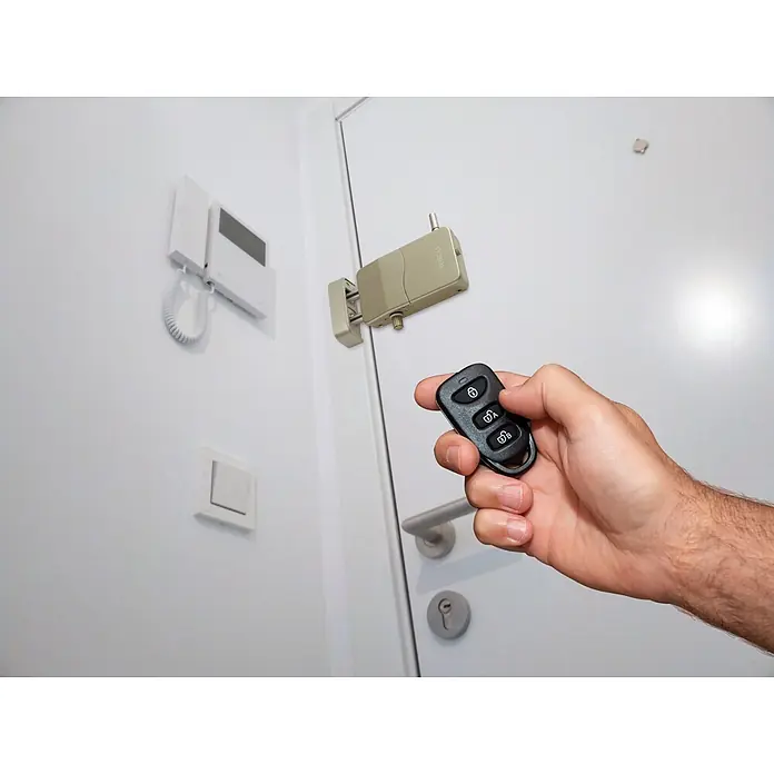 Arregui Cerradura electrónica CI10 - Dorado, Apto para: Puertas, Señal de alarma: 110 dB - Cerradura de puerta electrónica dorada con control remoto negro sostenido por una mano, mostrando acceso inteligente.