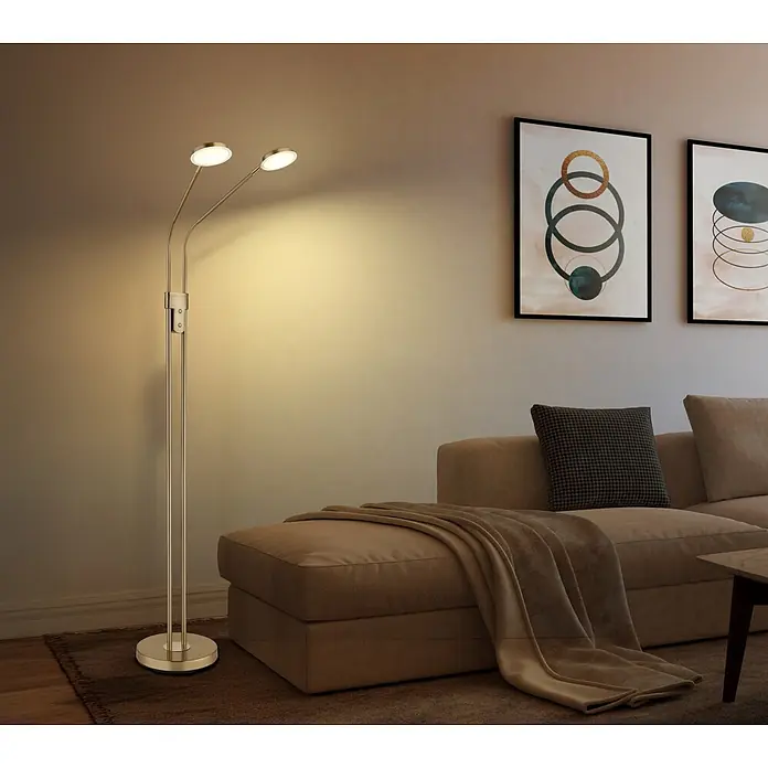 Globo LED-Deckenfluter Silvio - 6,5 W, Höhe: 1.730 mm - Goldene Stehleuchte mit zwei Köpfen beleuchtet eine Wand im Wohnzimmer neben einem braunen Sofa.