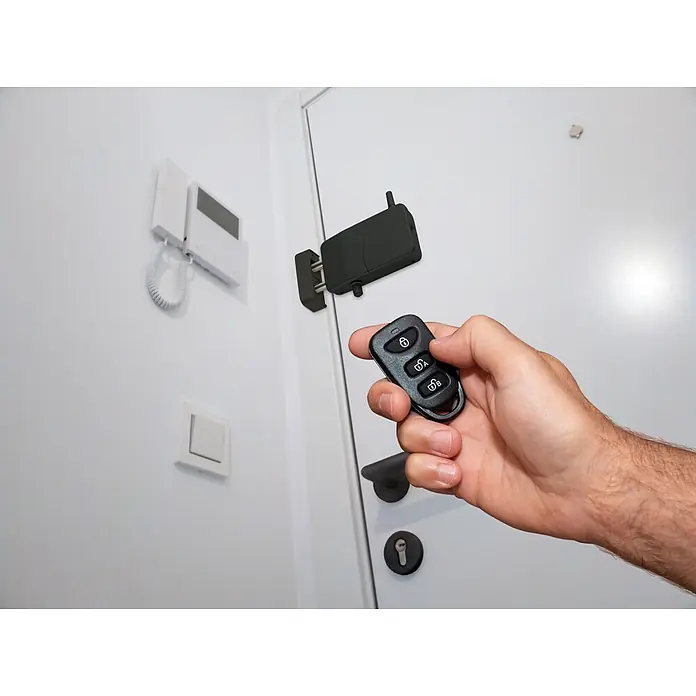 Arregui Cerradura electrónica CI10 - Negro, Apto para: Puertas, Señal de alarma: 110 dB - Una mano sostiene un control remoto negro, apuntándolo a una cerradura de puerta inteligente negra, demostrando el desbloqueo remoto.
