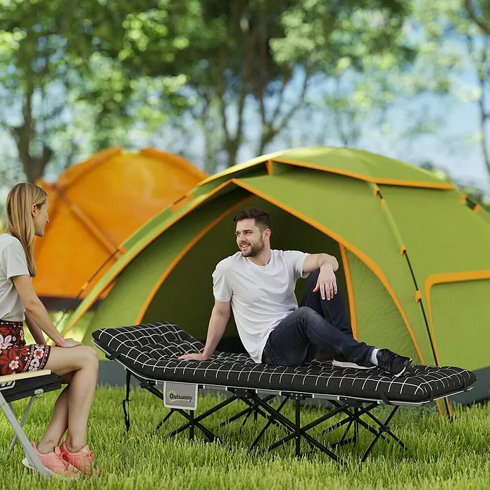 Outsunny Campingliege - Schwarz, Metall - Ein Mann entspannt auf einer schwarzen Campingliege mit weißem Karomuster, draußen bei Zelten aufgestellt.