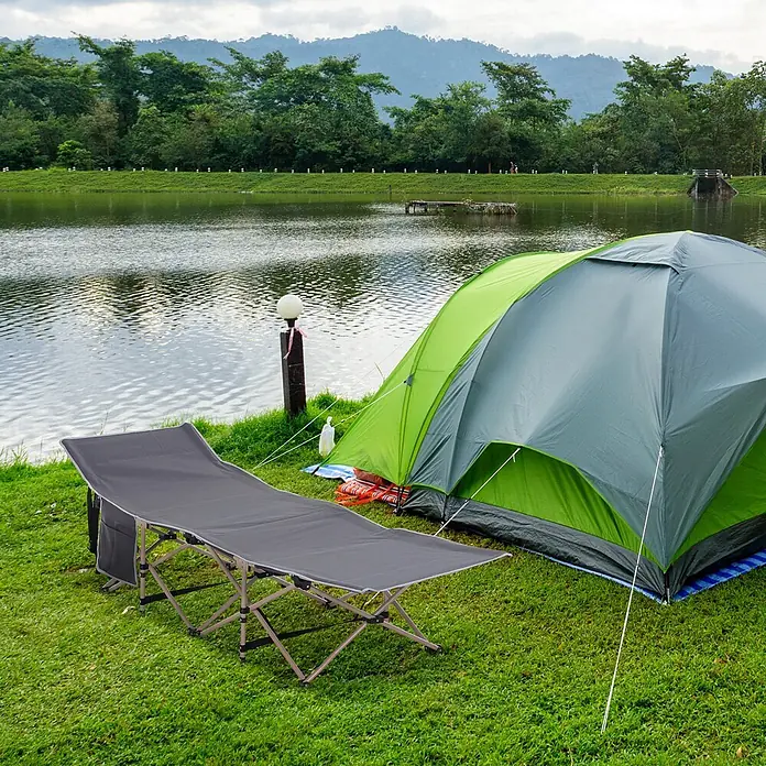 Outsunny Campingliege - Dunkelgrau, Stahl, Klappbar - Dunkelgraues Klappbett für Camping, draußen neben einem grünen Zelt am See aufgestellt, bereit zum Entspannen.