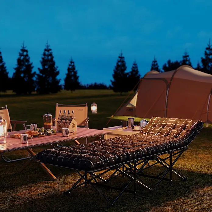 Outsunny Campingliege - Schwarz, Metall - Schwarz-weiß kariertes Feldbett nachts auf einem Campingplatz mit Zelt und Tisch.