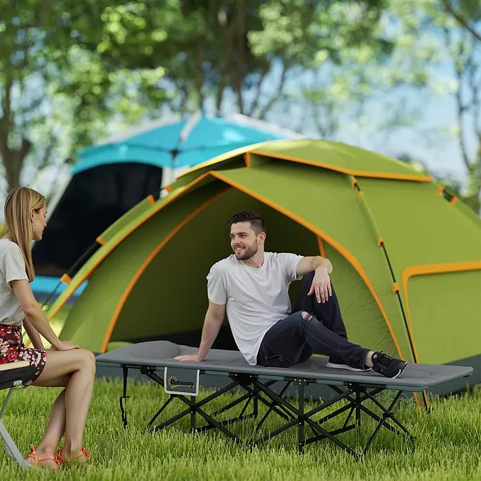 Outsunny Campingliege - Grau, Metall - Mann sitzt auf grauem Campingbett im Freien, Zelte im Hintergrund.