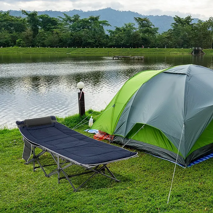 Outsunny Campingliege - Dunkelblau, Grau, Stahl - Ein dunkelblaues Feldbett mit grauem Gestell steht auf Gras neben einem grün-grauen Zelt am See.