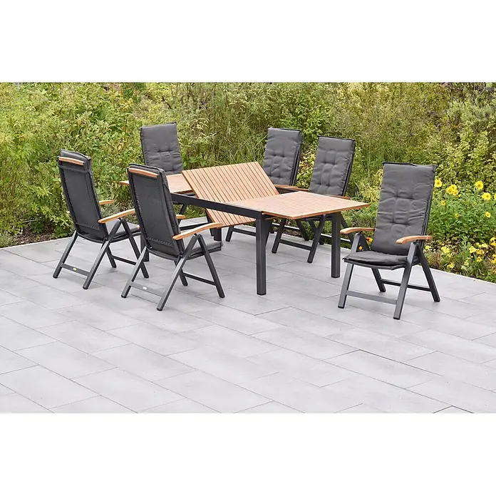 Merxx Gartentisch-Set Tilos - Gesamtumfang: 13 -tlg., Aluminium/Akazie, Klappbar - Ausziehbarer Outdoor-Esstisch mit Holzlattenplatte, dunkelgrauem Metallrahmen und sechs Stühlen mit dunkelgrauen Kissen und Holzarmlehnen auf einer Terrasse.