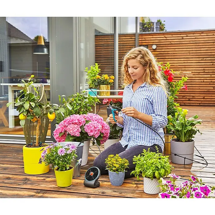 Gardena Bewässerungssteuerung AquaBloomSolarbetrieben - Frau installiert ein Gardena Micro-Drip-System zur Bewässerung von Pflanzen auf einer Holzterrasse.