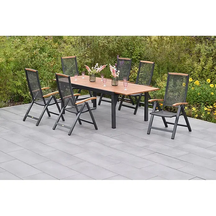Merxx Gartentisch-Set Tilos - Gesamtumfang: 7 -tlg., Aluminium/Akazie, Klappbar - Garten-Essgruppe mit dunklem Metallgestell, Holztischplatte und dunklen Netzstühlen mit Holzarmlehnen, auf einer Terrasse im Garten.
