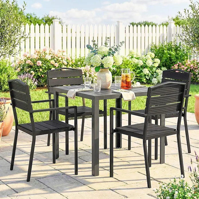 Outsunny Gartenstuhl-Set - 4 Stk., Polyethylen hoher Dichte (HDPE), Stapelbar, Schwarz - Ein dunkelgraues Terrassen-Essgarnitur mit quadratischem Tisch und vier Stühlen auf einer gepflasterten Terrasse in einem üppigen Garten.