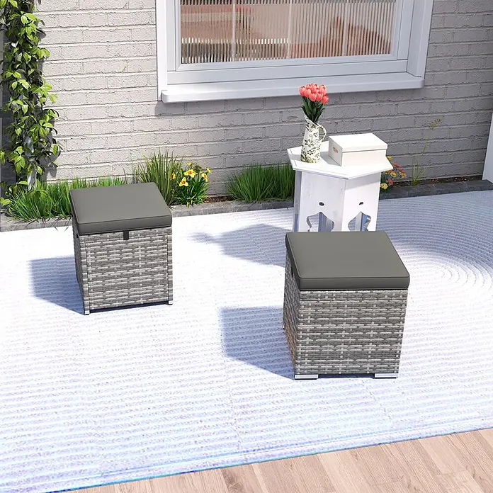 Outsunny Gartenhocker - Dunkelgrau - Zwei graue Rattan-Outdoor-Aufbewahrungshocker mit dunkelgrauen Kissen auf einer Terrasse.