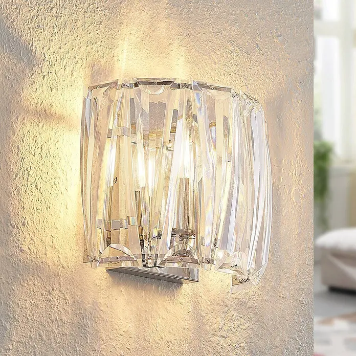 Lindby Wandleuchte Sofia - L x B x H: 14 x 23 x 20 cm, klar / transparent, E14 - Kristall-Wandleuchte mit Chromsockel, strahlt warmes Licht auf einer strukturierten Wand aus.