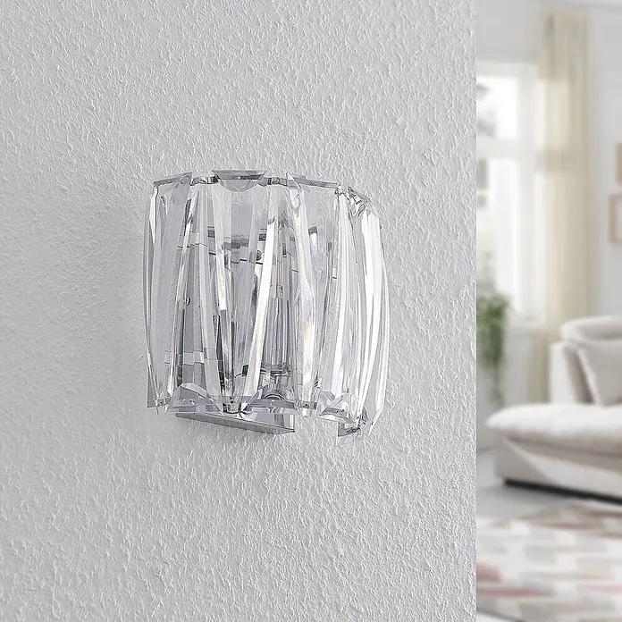 Lindby Wandleuchte Sofia - L x B x H: 14 x 23 x 20 cm, klar / transparent, E14 - Elegante Wandleuchte aus facettiertem Klarglas mit Chromfuß, an einer strukturierten Wand im Wohnzimmer.