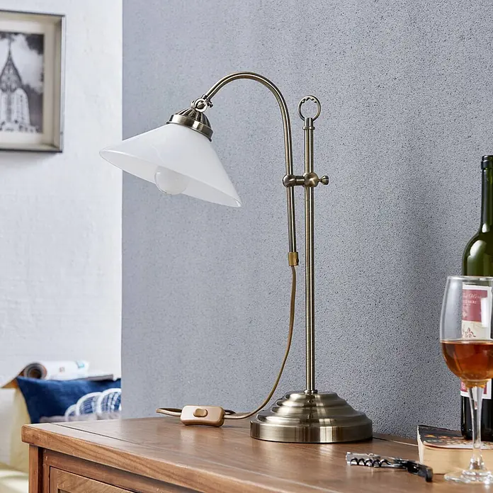 Lindby Tischleuchte Otis - bronze / altmessing, E14 - Verstellbare Tischlampe mit antikem Messing-Finish, weißem Glasschirm und Schnurschalter auf Holztisch.
