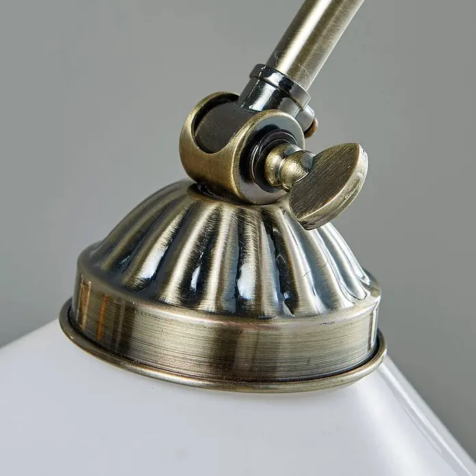 Lindby Tischleuchte Otis - bronze / altmessing, E14 - Nahaufnahme einer antiken Messinglampenverbindung und geriffelten Basis, die mit einem weißen Lampenschirm verbunden ist.