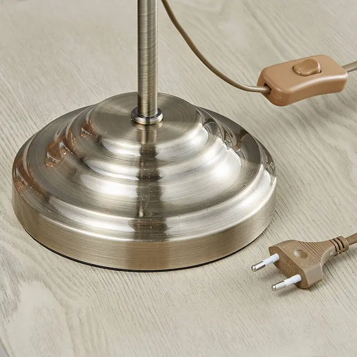 Lindby Tischleuchte Otis - bronze / altmessing, E14 - Lampenfuß in Bronzeoptik mit braunem Stromkabel, Schalter und zweipoligem Eurostecker auf heller Holzoberfläche.