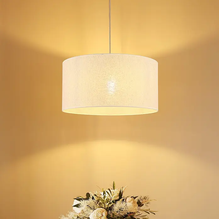 Globo Pendelleuchte Jule - 60 W, Ø x H: 50 x 120 cm - Beleuchtete weiße Stoff-Hängeleuchte in Trommelform, die ein warmes Licht über ein Blumenarrangement wirft.