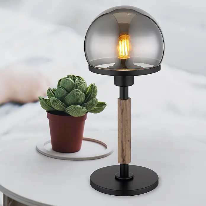 Globo Tischleuchte Haku - 40 W, Höhe: 400 mm, E27 - Eine stilvolle Tischlampe mit schwarzem Fuß, Holzstielakzent und Rauchglas-Schirm, leuchtet neben einer Sukkulente auf einem hellen Tisch.