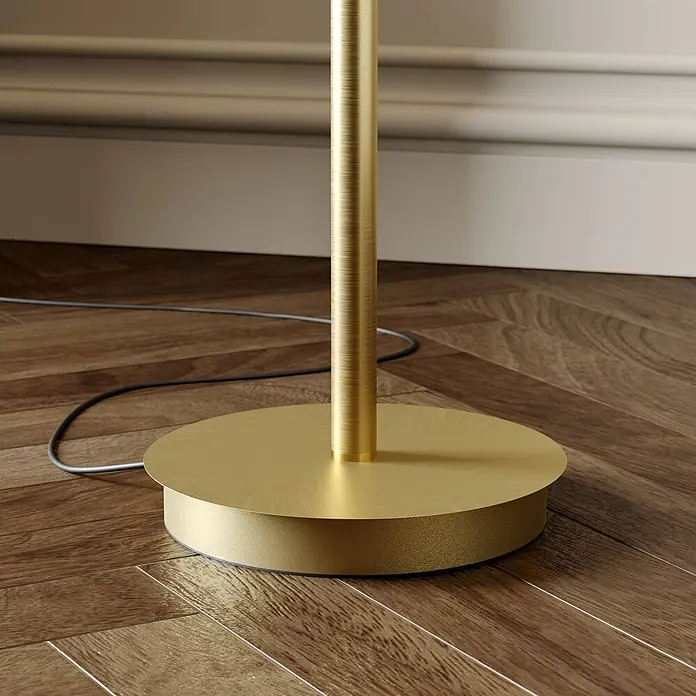 Lucande LED-Deckenfluter Anniki - Höhe: 180 cm, messing / gold, messing / gold, Warmweiß - Goldene Stehleuchtenbasis und Stange auf Holzboden an einer Wand, mit sichtbarem Stromkabel.