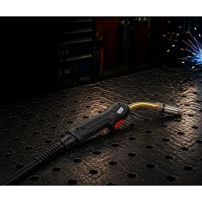 EWM MIG/MAG-Schweißbrenner UM 36 gasgekühlt 5m - 5 m - Ein schwarzer und goldener Schweißbrenner liegt auf einem Metallschweißtisch in einer Werkstatt, im Hintergrund sind Schweißfunken sichtbar.