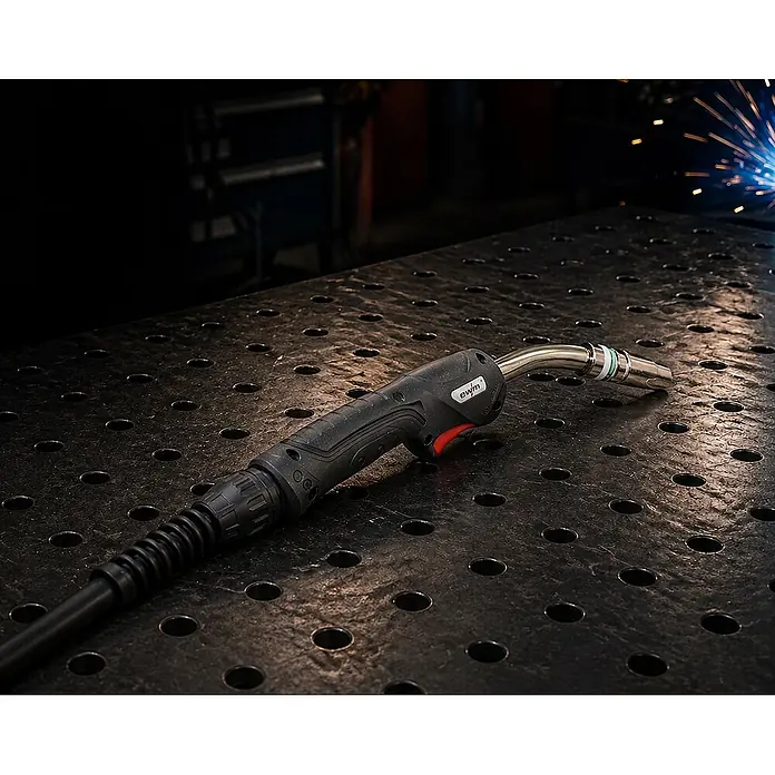 EWM MIG/MAG-Schweißbrenner UM 25 gasgekühlt 5m - 5 m - Schwarzer und metallischer Schweißbrenner auf dunkler, gelochter Metallwerkbank mit Schweißfunken im Hintergrund.