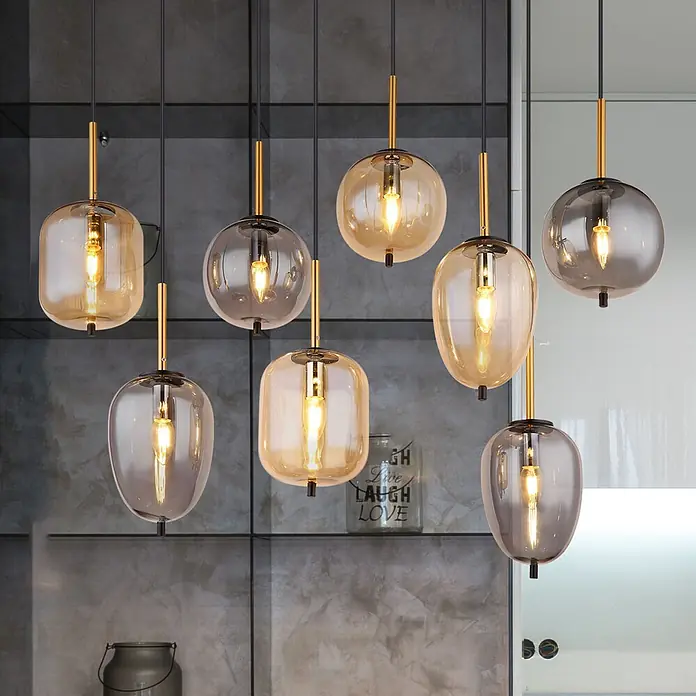 Globo Pendelleuchte Tulivar - 40 W, L x B x H: 1.025 x 340 x 1.200 mm - Mehrere Pendelleuchten mit bernsteinfarbenen und rauchfarbenen Glasschirmen, Messingakzenten, in einem modernen Raum.