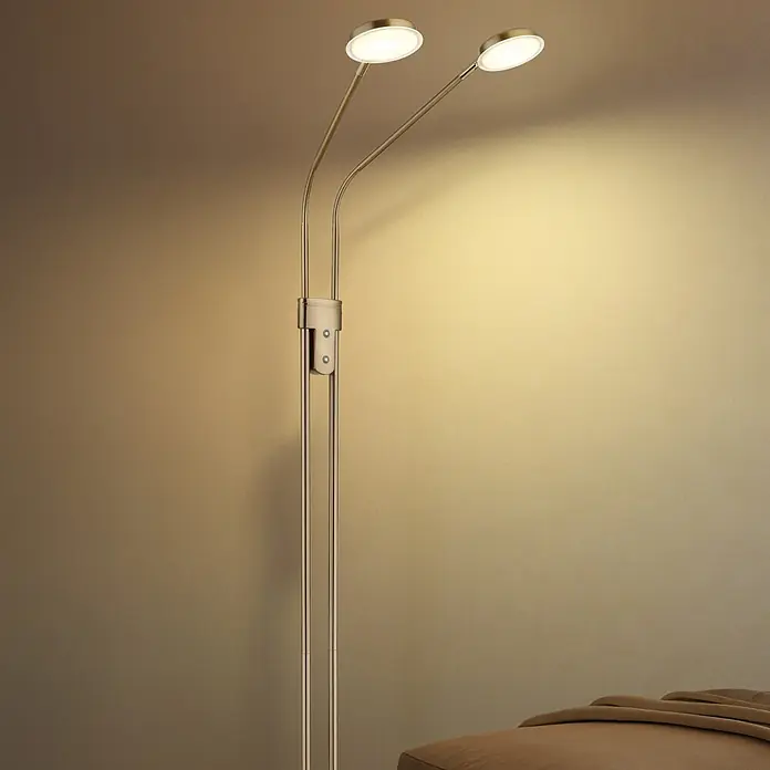Globo LED-Deckenfluter Silvio - 6,5 W, Höhe: 1.730 mm - Zweiflammige Stehleuchte aus gebürstetem Messing-Metall, beleuchtet eine Wand und ein Möbelstück in gemütlicher Umgebung.