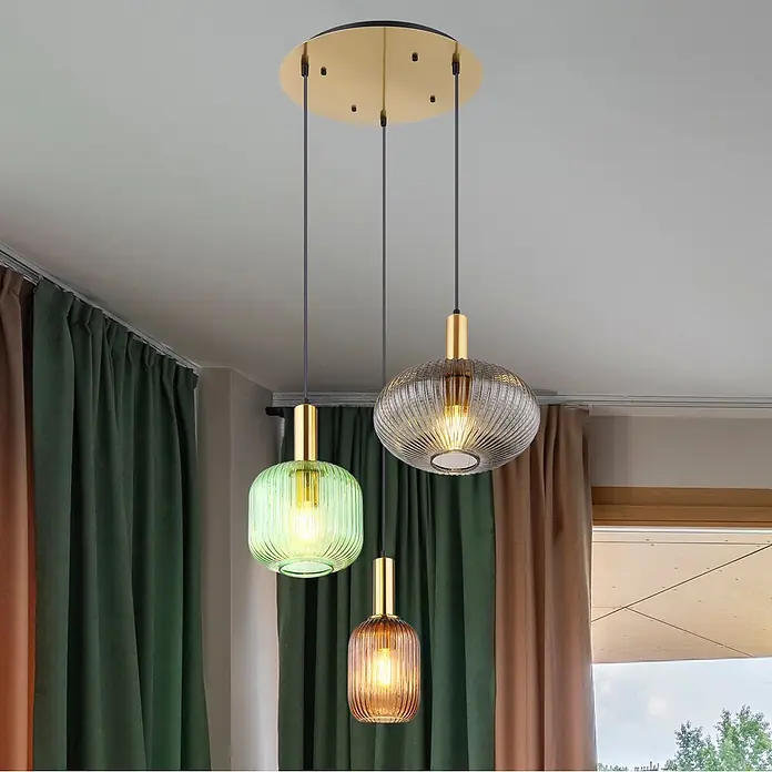Globo Pendelleuchte Tulivar - Höhe: 1.300 mm, 60 W - Eine dreiflammige Pendelleuchte mit gerippten grünen, bernsteinfarbenen und rauchfarbenen Glasschirmen und goldener Deckenplatte, hängt in einem Raum.