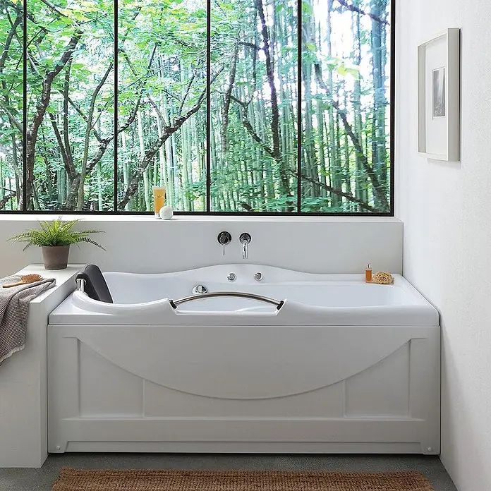 Kiamami Valentina Badewanne - 1.700 x 780 cm, ABS-Kunststoff und Acryl, Weiß - Weiße Badewanne mit integrierter Kopfstütze und Chromgriffen, vor einem großen Fenster mit Waldblick.