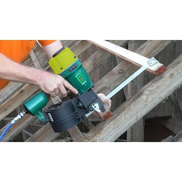 Prebena Druckluftnagler 8XR-CNW90 - Betriebsdruck: 5 bar - 8,3 bar, Passend für: Rundkopf-Coilnägel der Tye Typ CNW von 45 - 90 mm - Ein Mann verwendet ein Druckluftnagelgerät, um einen Nagel in ein Holzstück zu schlagen. Das Werkzeug ist grün, schwarz und gelb.